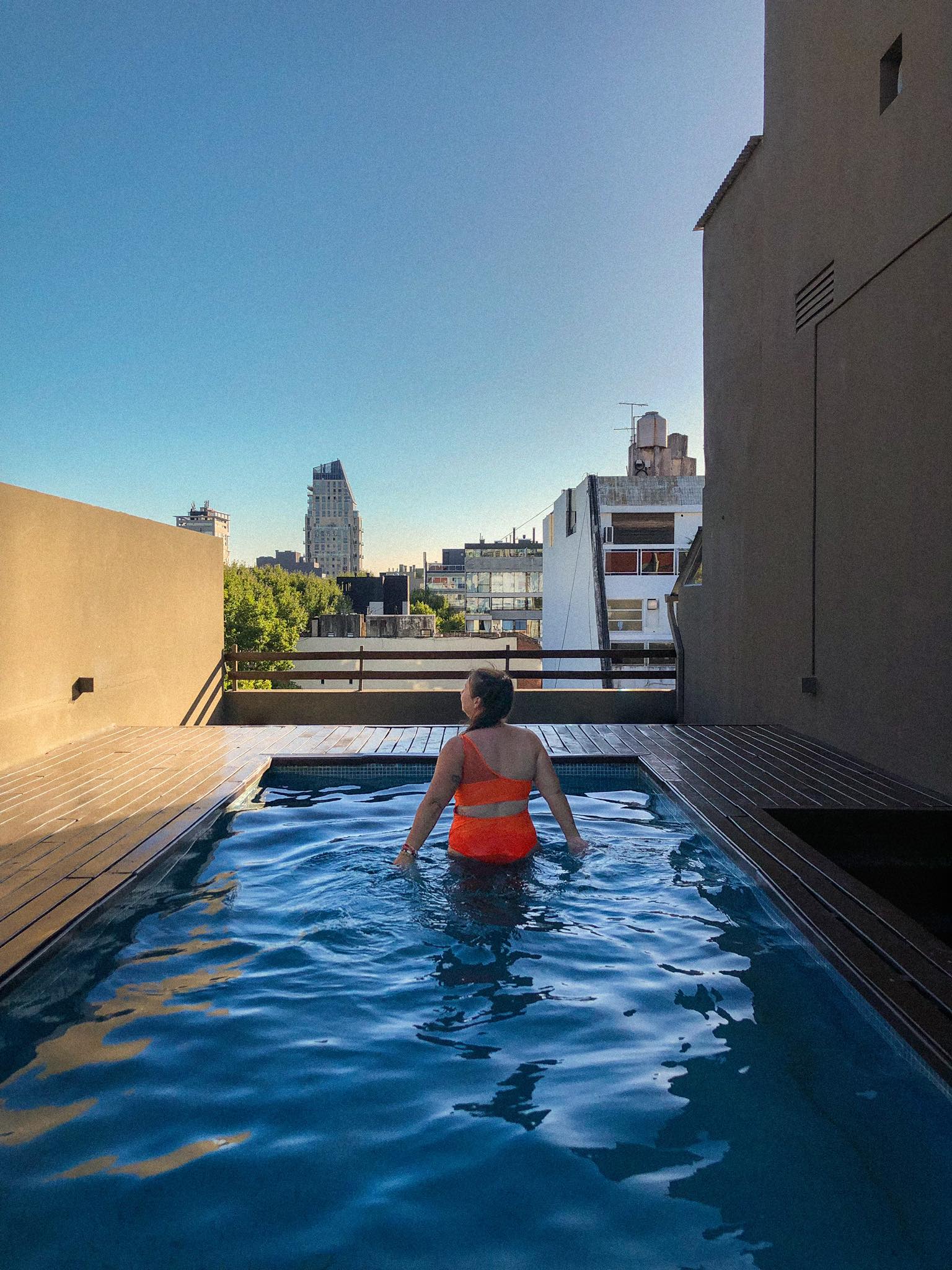 Une femme de dos avec un maillot orange dans une piscine sur le toit d'un immeuble 
